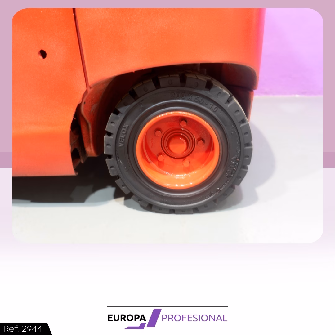 7 - EUROPA PROFESIONAL Close-up of a red toy vehicle wheel: black tread with an orange rim, mounted in a red body near a light floor and purple background.